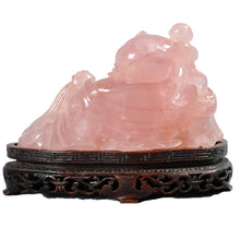 Load image into Gallery viewer, A carved rose quartz figurine of a reclining figure, displayed on an ornate dark brown carved wooden base. 